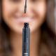 Het model is lachend op de achtergrond te zien, de geopende mascara staat in de focus