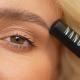Blonde vrouw die de Shape Mascara dicht bij haar voorhoofd houdt