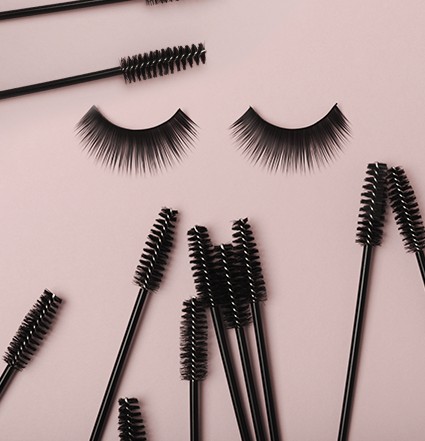 Twee wimpers in het midden, omgeven door mascara-staafjes op een roze achtergrond