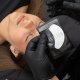 Een persoon die een wimperverlengingsbehandeling krijgt van een technicus die zwarte handschoenen draagt.